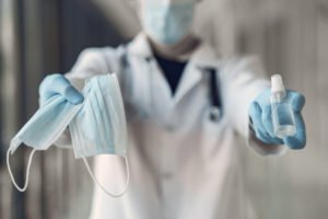 Manos sostienen una mascarilla y un frasco desinfectante