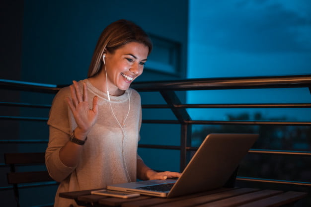 mujer-sonriente-joven-que-tiene-llamada-video-usando-computadora-portatil-noche_109710-851