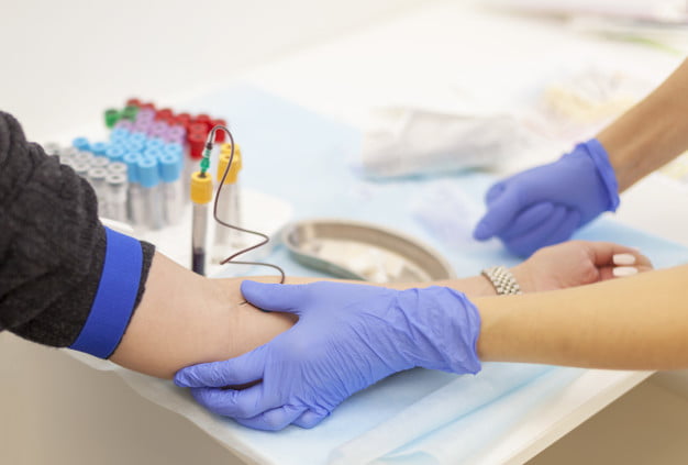A doctor in blue gloves takes blood from a vein from a young woman. Several test tubes. Diagnosis, disease, examination concept.