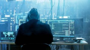 Persona encapuchada frente a varias pantallas de computadora