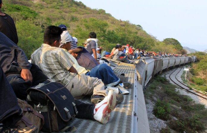 migracion 3 Personas esperan sentadas junto a una carretera