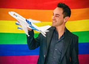 Hombre sostiene un avión en miniatura frente a una bandera arcoíris