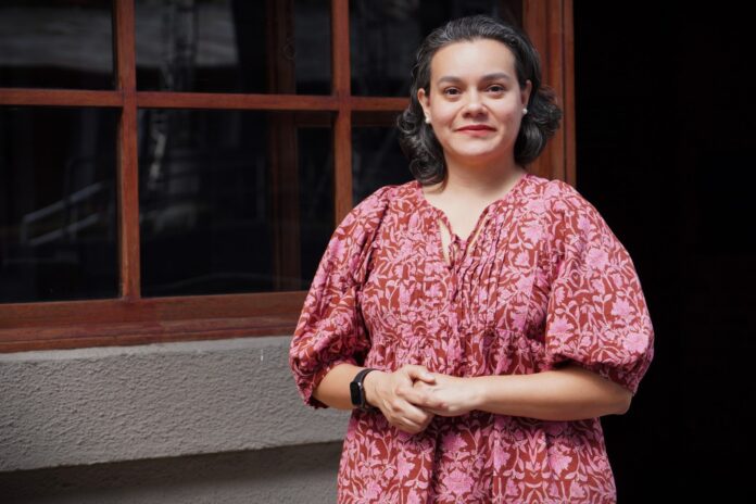 Ministerio de cultura y juventud Mujer habla frente a una casa de madera